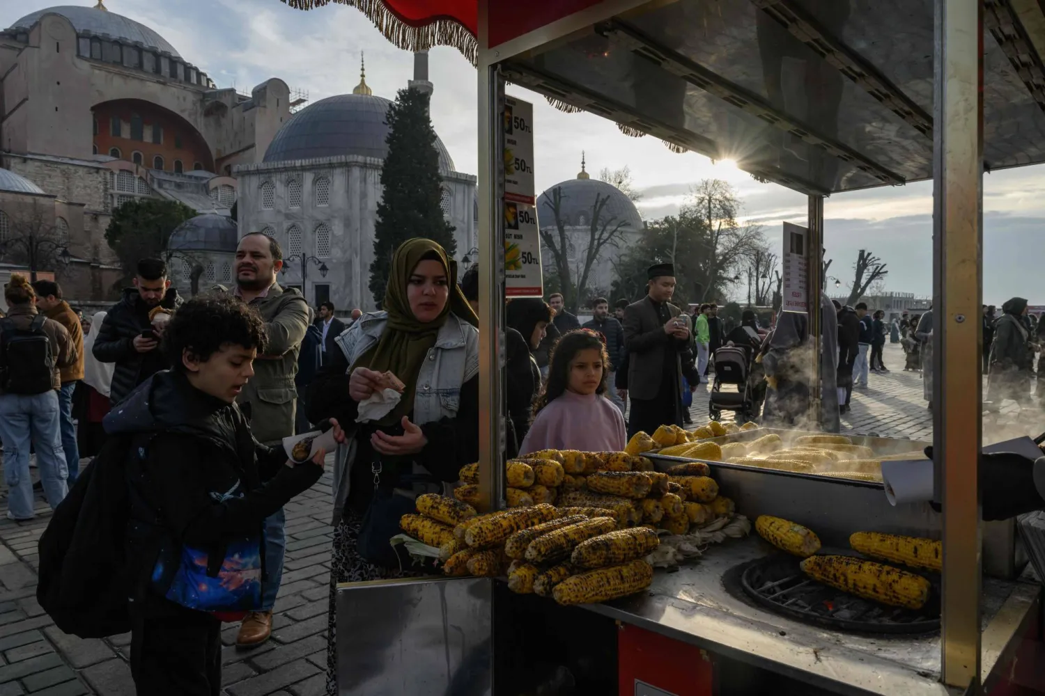 أم وأولادها يشترون الذرة من بائع متجول في إسطنبول (أ.ف.ب)