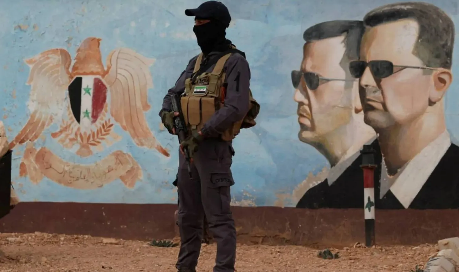 A member of Hayat Tahrir al-Sham stands guard near an image of Syria's Bashar al-Assad at the fourth division headquarters in Damascus, Syria, January 23, 2025 (Reuters)