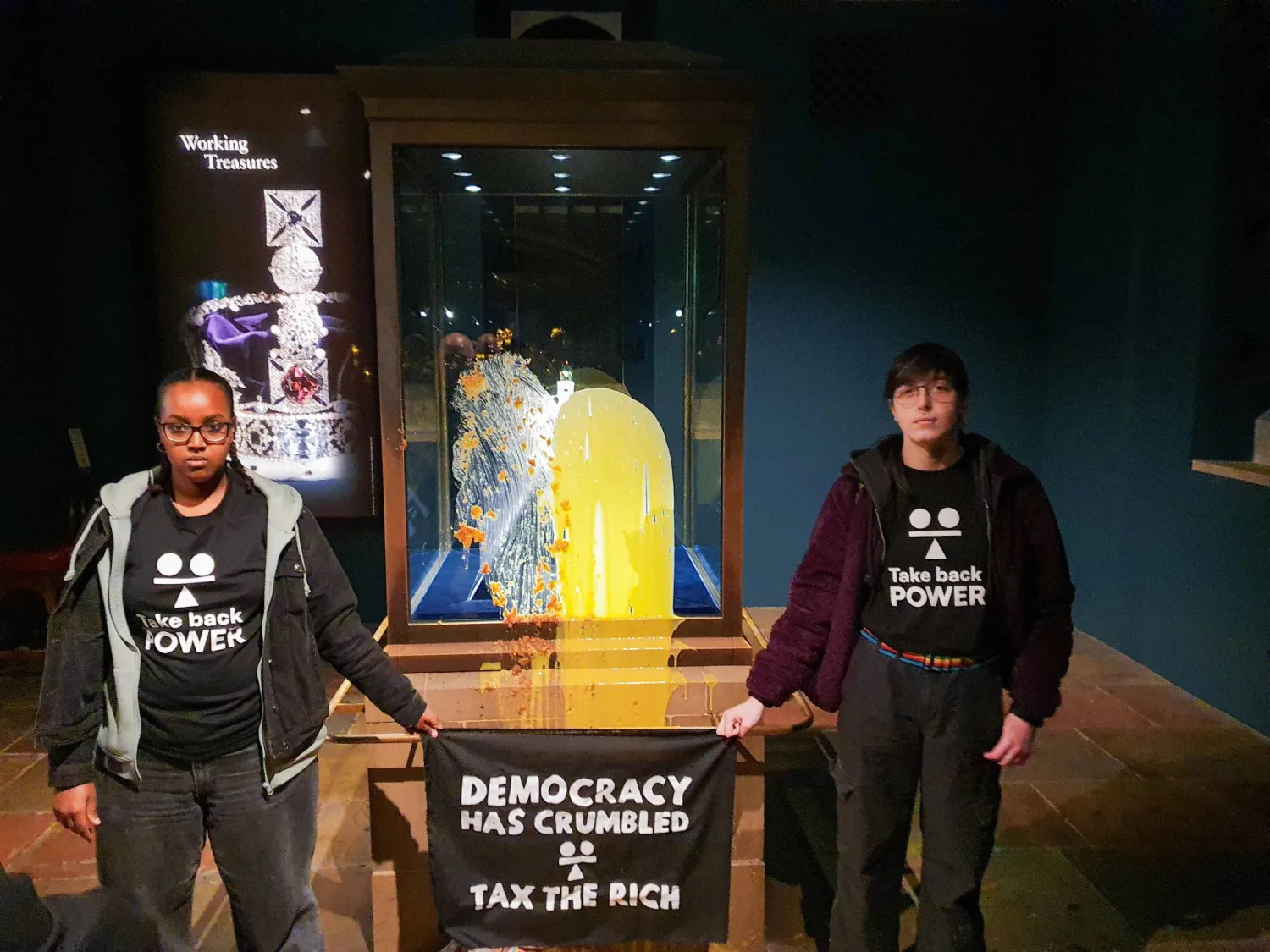 Members of an organization called Take Back Power hold a sign as they stand after they threw food at a display case containing the Imperial State Crown, at Tower of London, in London, Britain, December 6, 2025. TAKE BACK POWER/Handout via REUTERS 