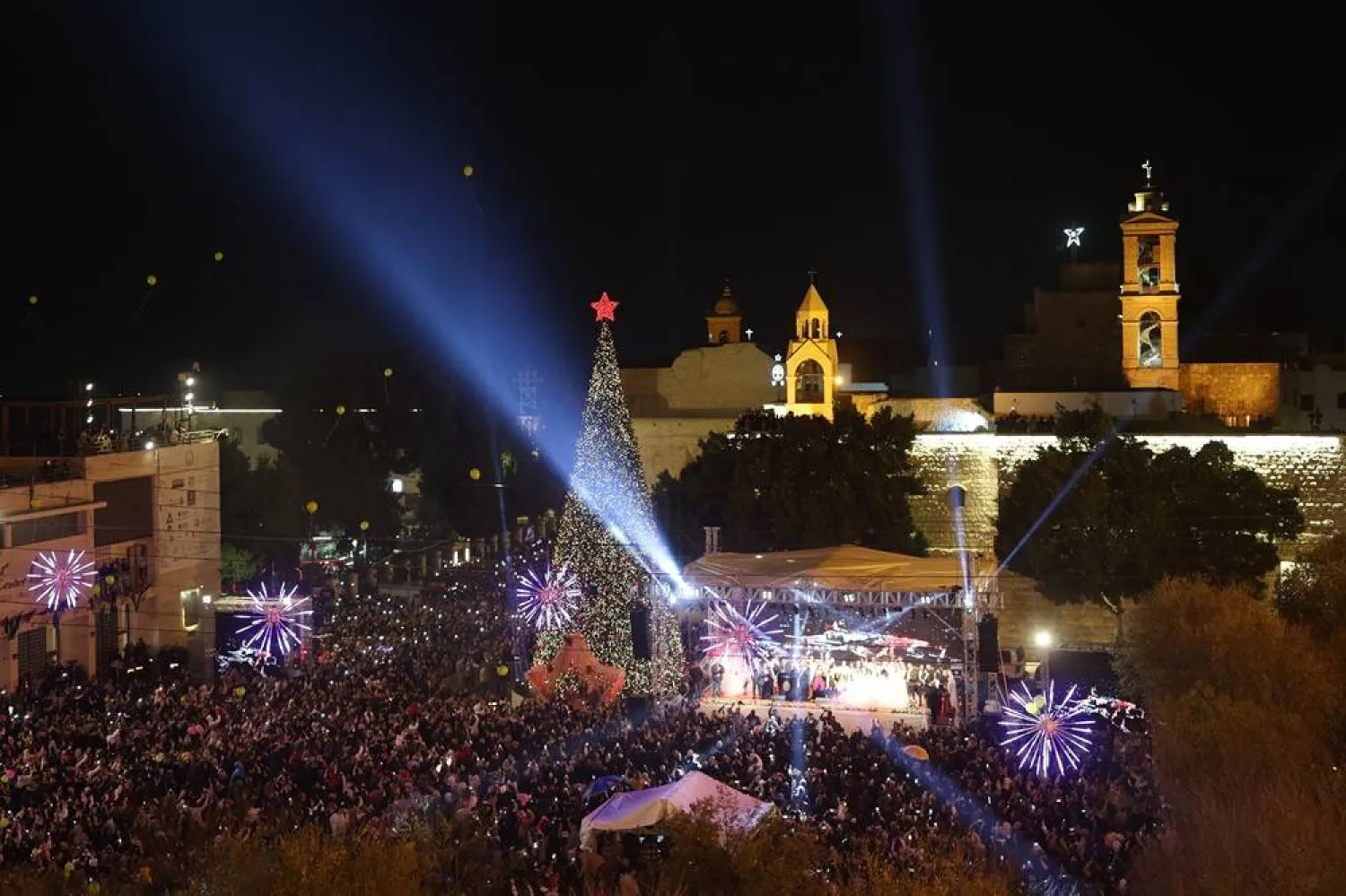 People gather during the lighting of the Christmas tree ceremony at the Manger Square, next to the Church of Nativity in the background, in the West Bank city of Bethlehem, 06 December 2025. (EPA)
