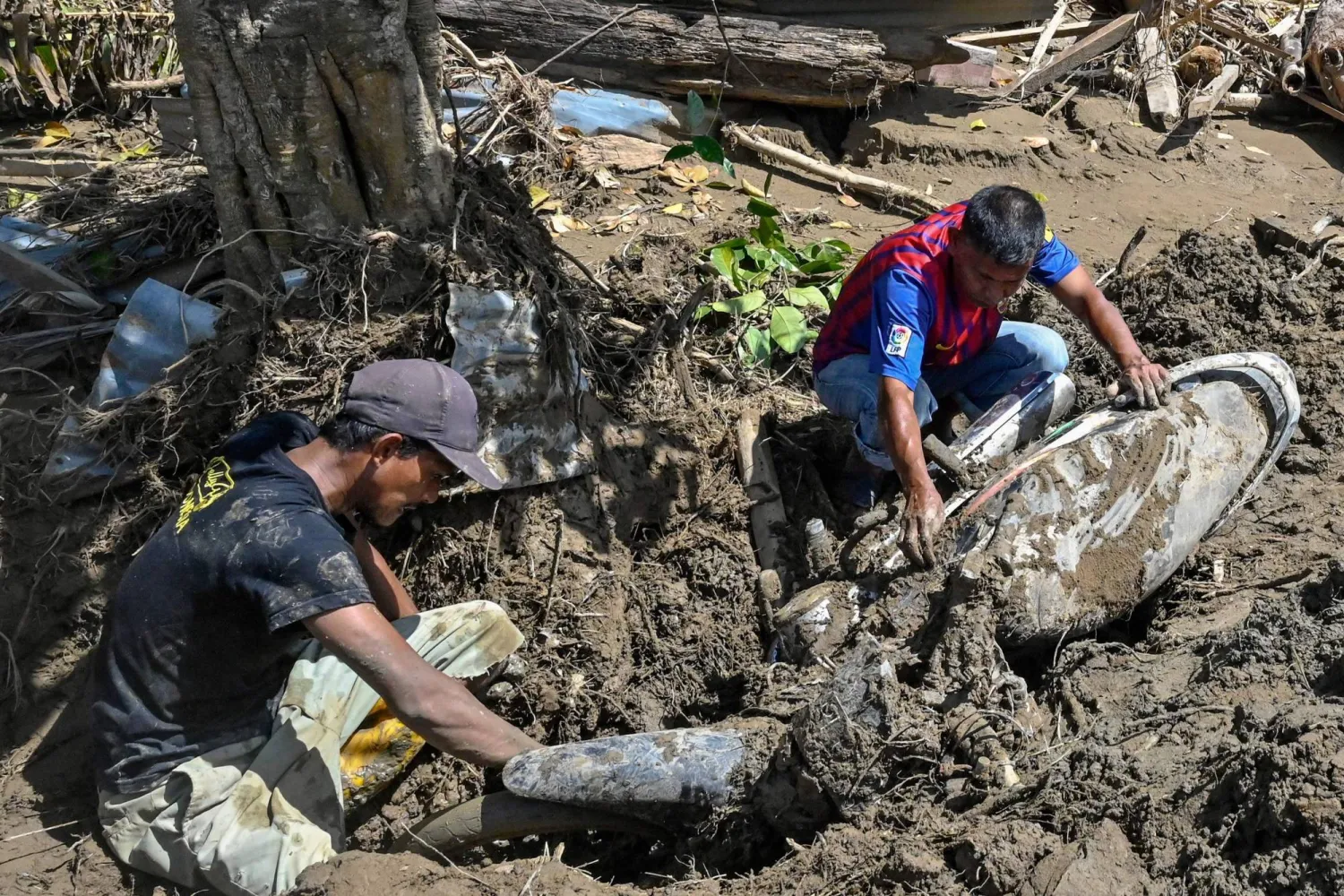 أشخاص يزيلون الطين من دراجة نارية إثر فيضانات مفاجئة في ميوريدو بمقاطعة بيدي جايا - إقليم آتشيه الإندونيسي (أ.ف.ب)