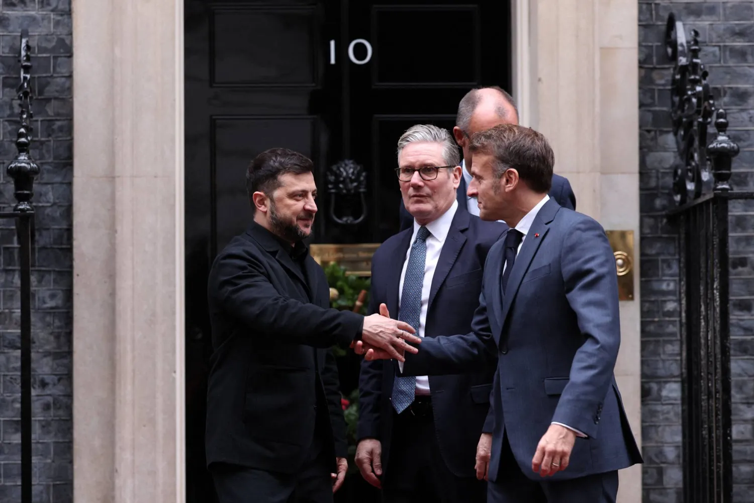 زيلينسكي يصافح الرئيس الفرنسي إيمانويل ماكرون بعد اجتماع مع رئيس الوزراء البريطاني كير ستارمر والمستشار الألماني فريدريش ميرتس في لندن الاثنين (رويترز)