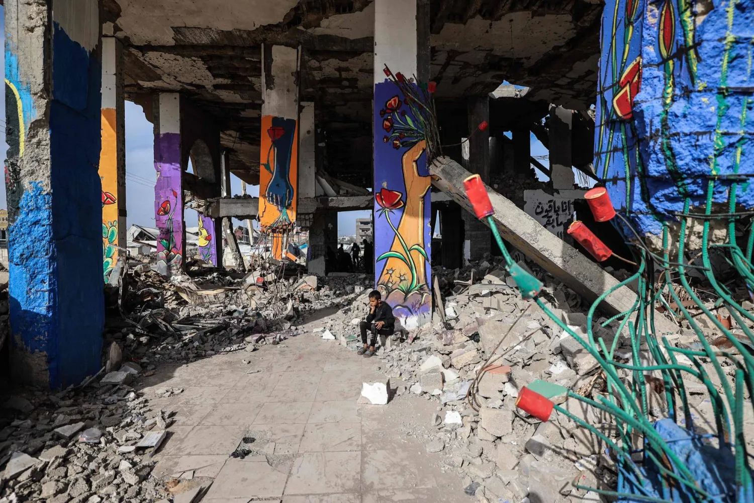 A boy sits amid murals painted on a destroyed building in the Maghazi refugee camp outside Deir al-Balah on December 8, 2025. (AFP)
