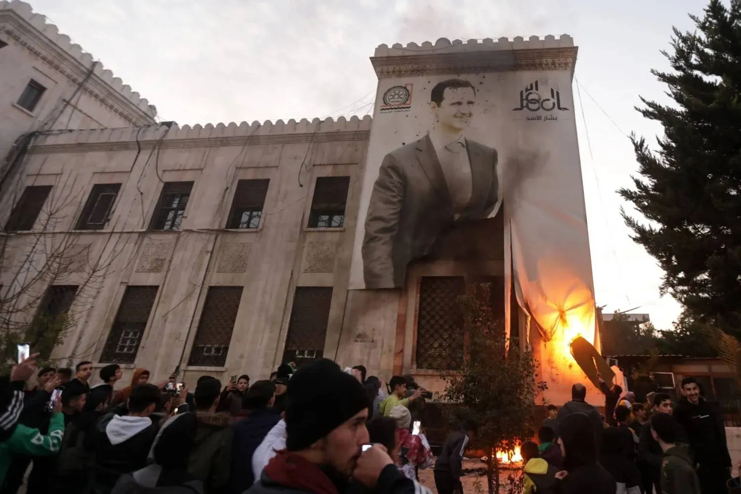 Hama residents set fire to a large banner of Bashar al Assad after armed factions seized the city last December (AFP)