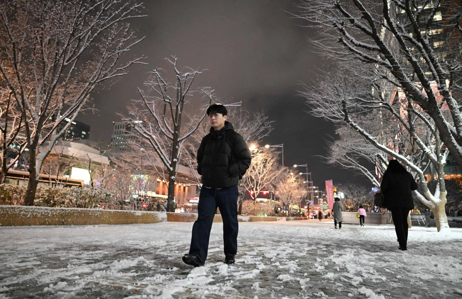 Pedestrians walk on a snowy street as the season's first snow falls in downtown Seoul on December 4, 2025. (AFP)