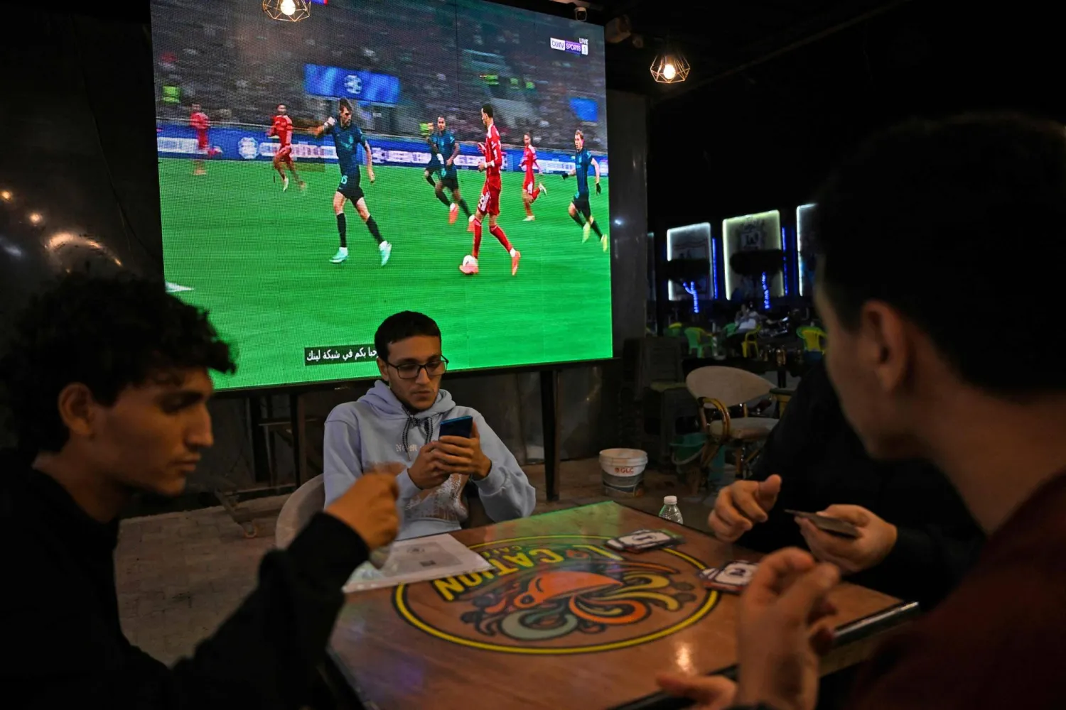 في أحد المقاهي يفضل المشجعون مطالعة هواتفهم بدلاً من مشاهدة الفريق الإنجليزي يلعب (أ.ف.ب)