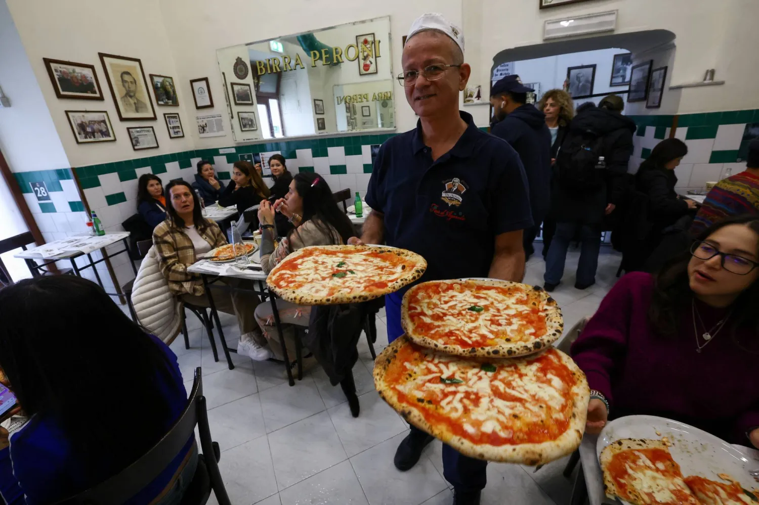 A waiter carries pizzas at L'antica Pizzeria da Michele as Italian cuisine awaits a crucial UNESCO decision that could recognize it as an Intangible Cultural Heritage of Humanity in Naples, Italy, December 5, 2025. (Reuters)