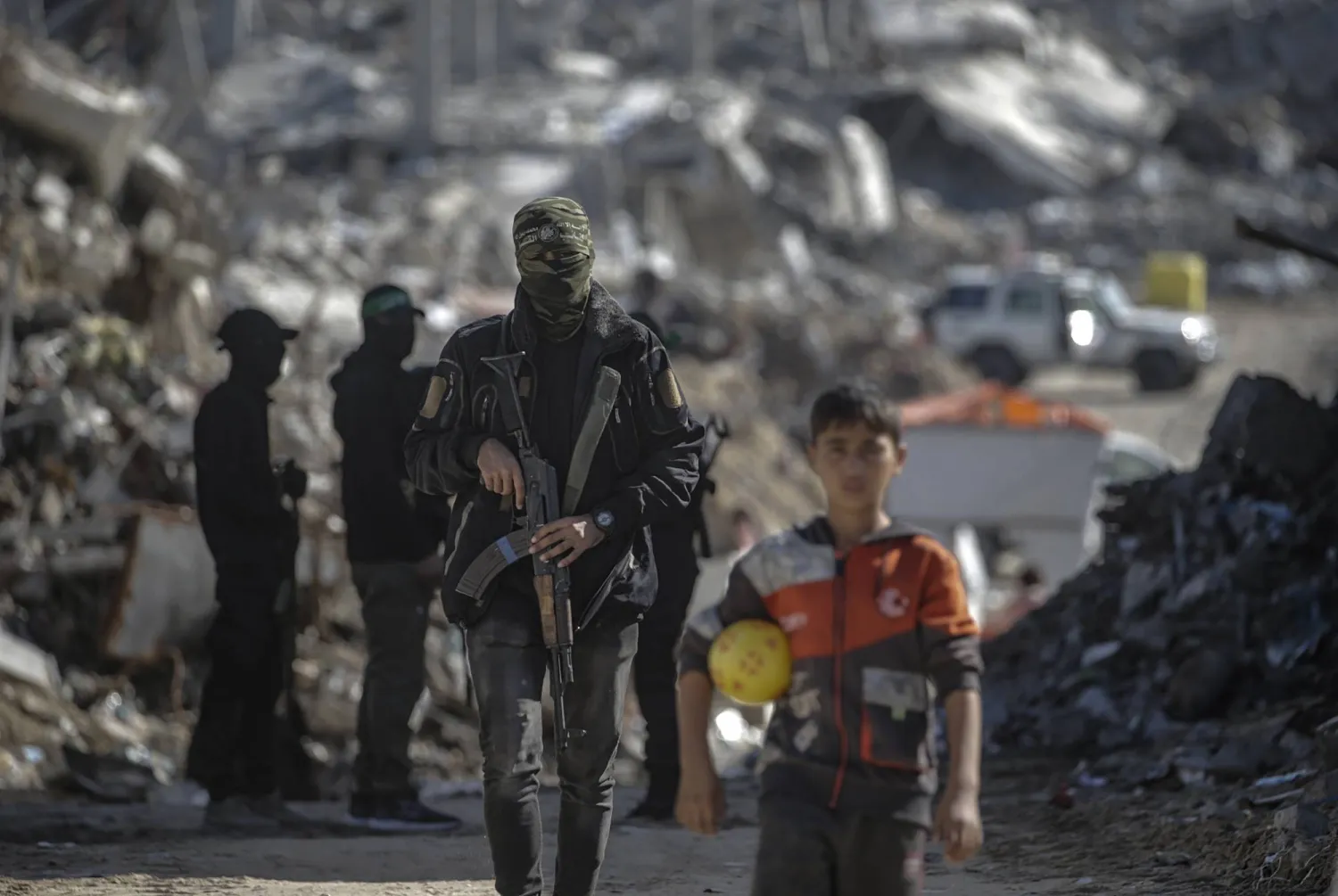 طفل فلسطيني يقف خلفه مقاتلون من «كتائب القسام» التابعة لـ«حماس» أثناء بحثهم عن جثث رهائن إسرائيليين في مخيم جباليا شمال غزة الاثنين (إ.ب.أ)