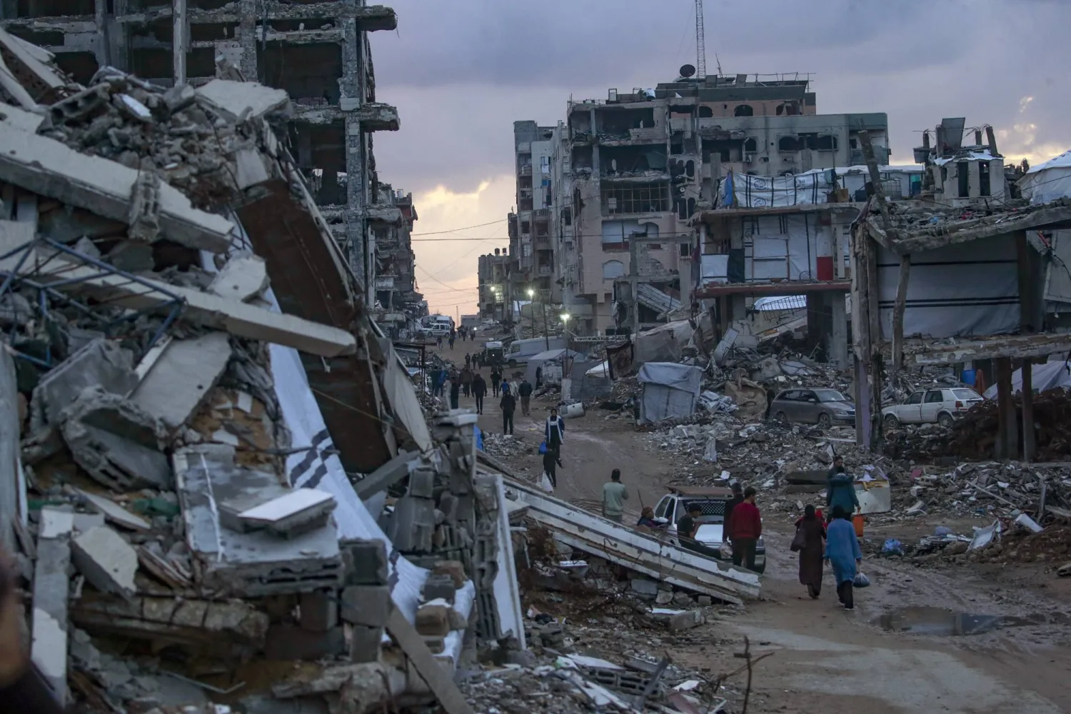 فلسطينيون نازحون يسيرون بين المباني المدمرة في حي الشيخ رضوان بمدينة غزة (إ.ب.أ)