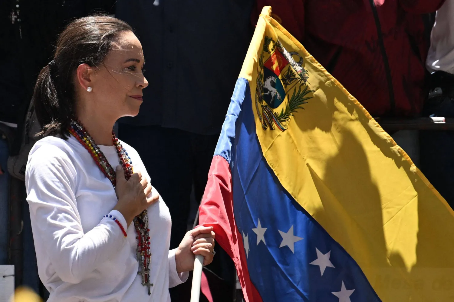 (FILES) Venezuelan opposition leader Maria Corina Machado holds a Venezuelan national flag as she gestures from atop a truck during a demonstration to protest over the presidential election results, in Caracas on August 3, 2024. (Photo by Juan BARRETO / AFP)