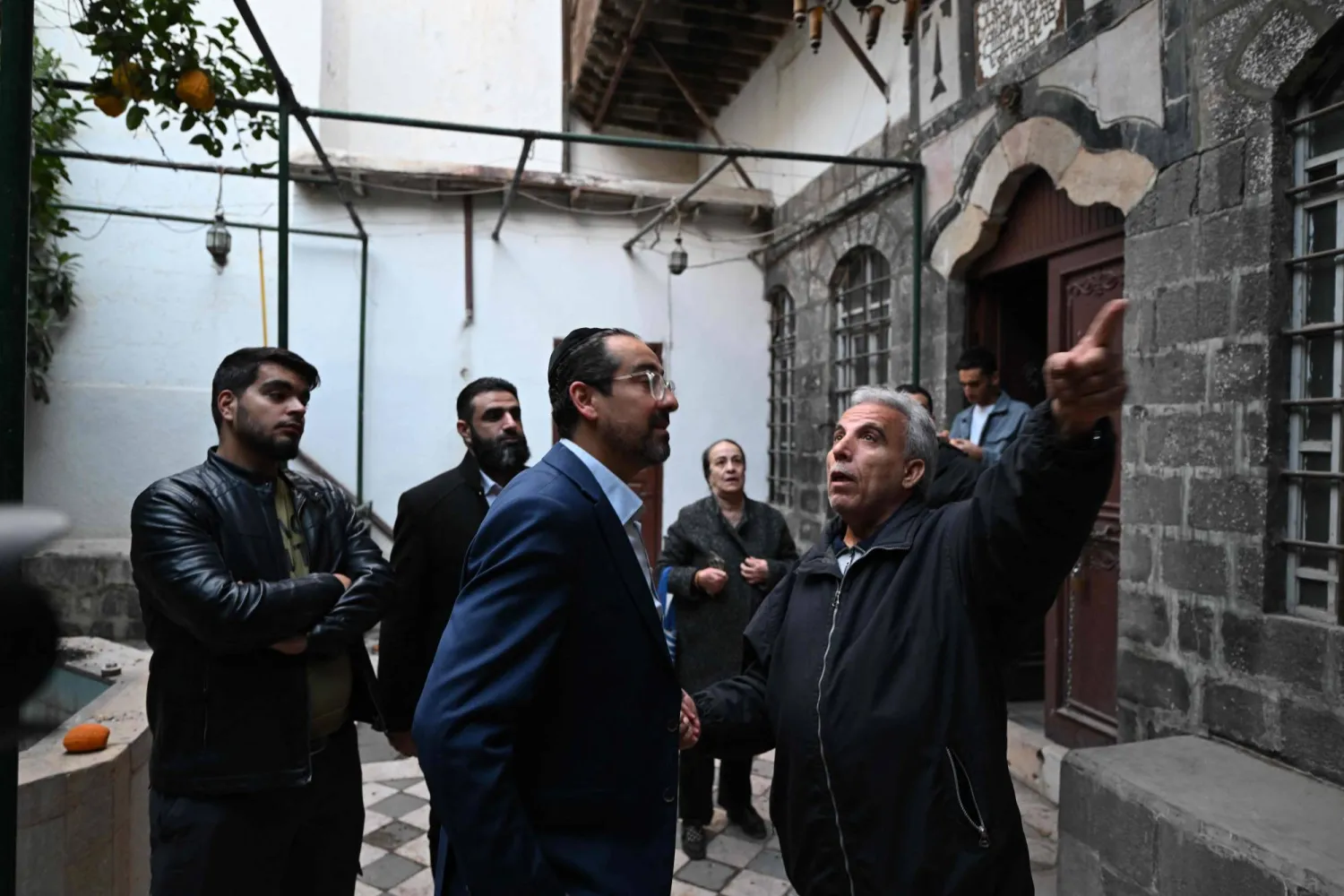 هنري حمرا (وسط) أحد الأعضاء المؤسسين لمنظمة يهودية سورية تُعنى باستعادة الممتلكات المصادرة في عهد الحكومات السورية السابقة أمام كنيس الفرنج في دمشق 10 ديسمبر (أ.ف.ب)