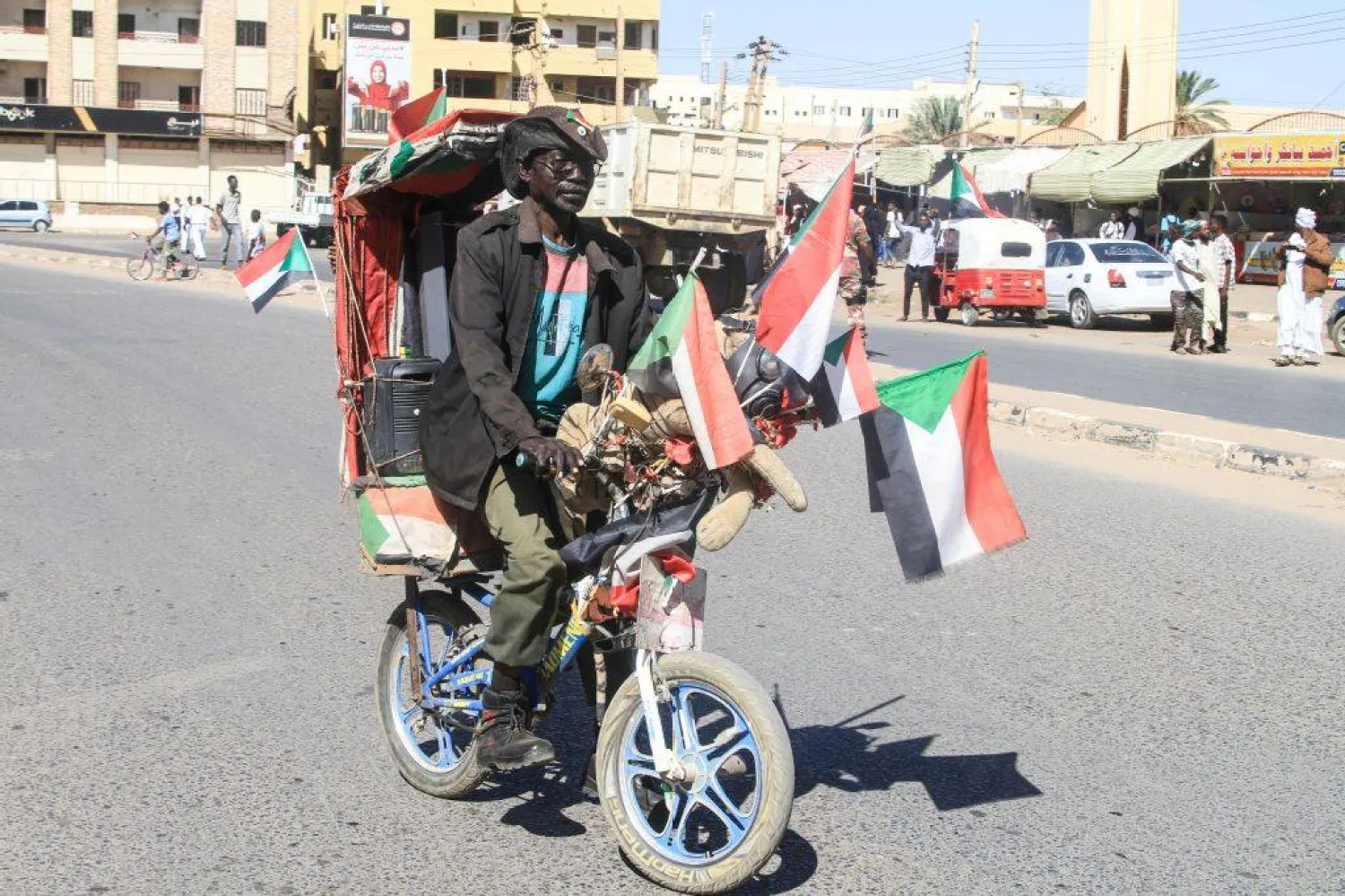 A Sudanese man rides his decorated bicycle as others (unseen) rally in support of the Sudanese armed forces. (Photo by Ebrahim Hamid / AFP)