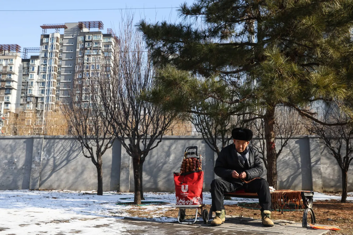 رجل مسن يجلس بجوار مبانٍ سكنية في العاصمة الصينية بكين (إ.ب.أ)