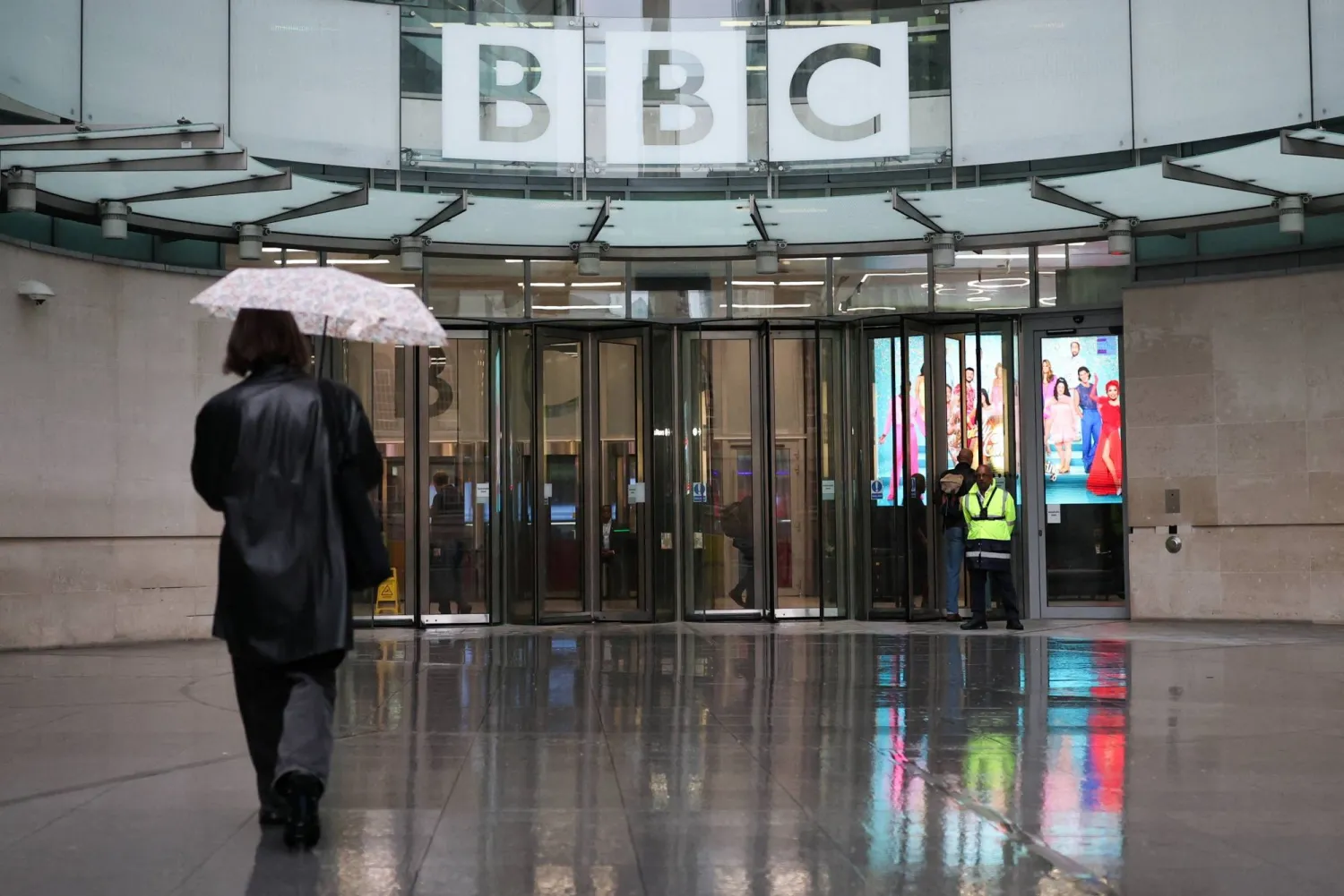 A person walks with an umbrella outside BBC Broadcasting House, after Director General Tim Davie and CEO of BBC News Deborah Turness resigned on Sunday, November 9, following accusations of bias at the British broadcaster, including in the way it edited a speech by US President Donald Trump, in London, Britain, November 14, 2025. REUTERS/Isabel Infantes