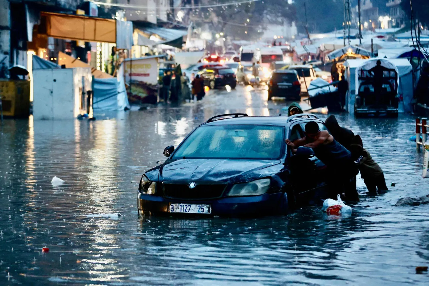 فلسطينيون نازحون يدفعون سيارة عبر مياه الفيضانات عقب هطول أمطار غزيرة في مدينة غزة (أ.ف.ب)