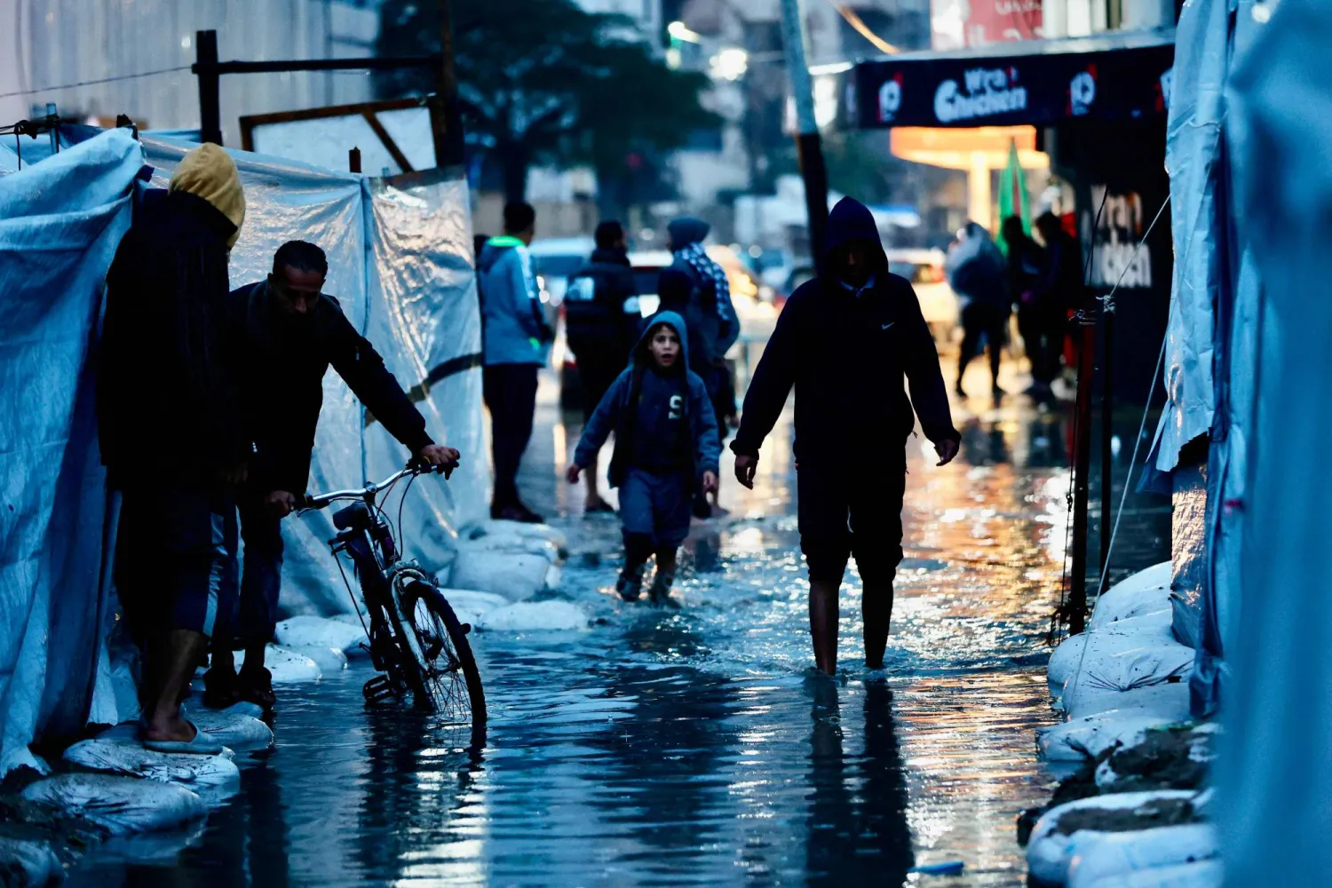 نازحون يمرون عبر برك المياه جراء الأمطار الغزيرة في مدينة غزة أمس (أ.ف.ب)