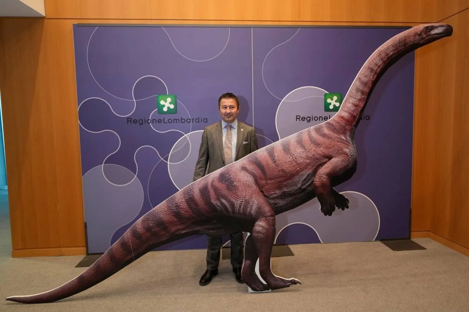 The Director of the Stelvio Park, Franco Claretti, poses next to a reproduction of a dinosaur prior to a press conference in Milan, Italy, Tuesday, Dec. 16, 2025, on a discovery of thousands of dinosaur tracks at the Stelvio Park. (AP) 