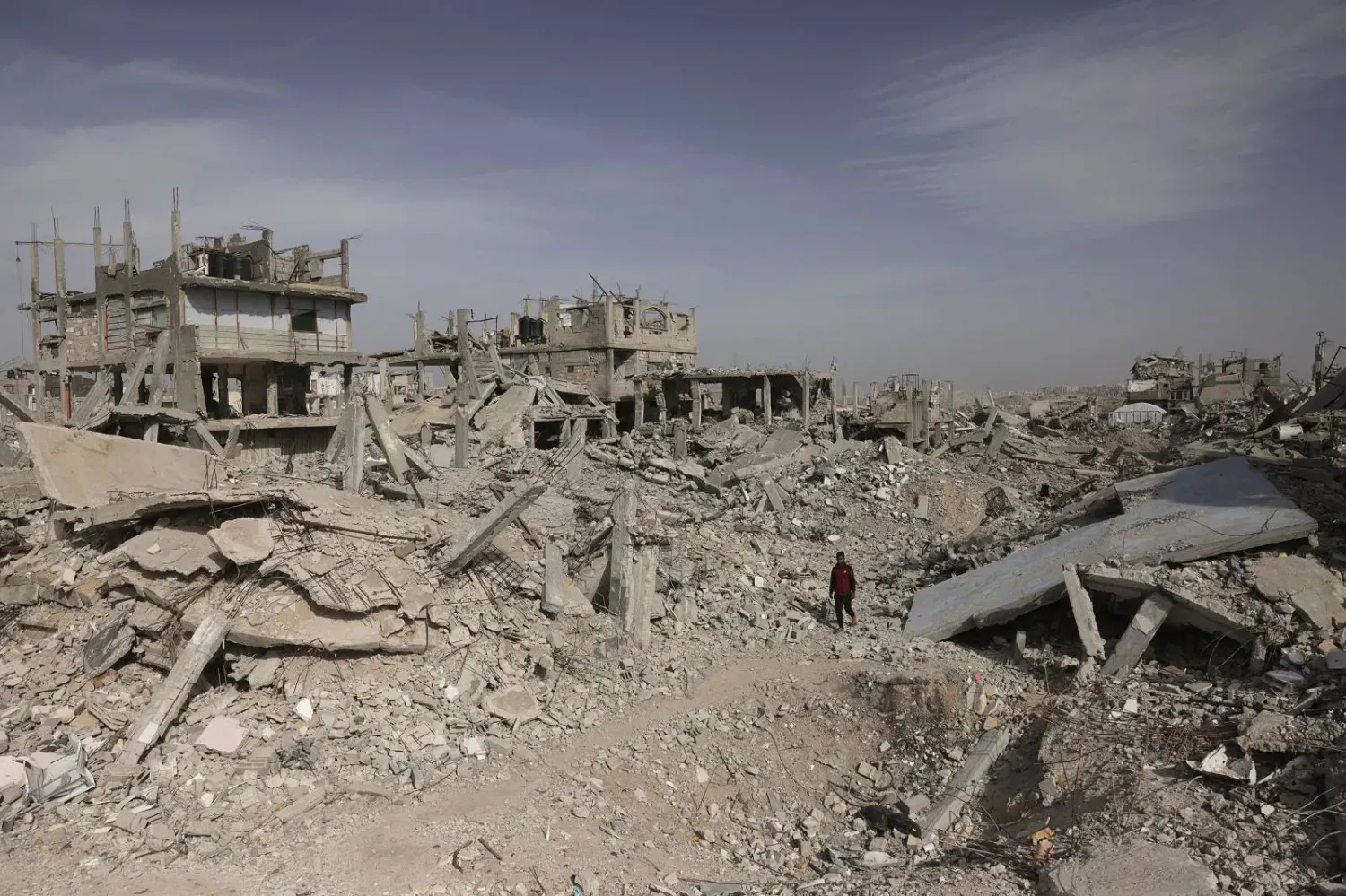 Gazze Şeridi'nin güneyindeki yıkılmış binaların enkazı arasında yürüyen Filistinli bir adam (AFP)