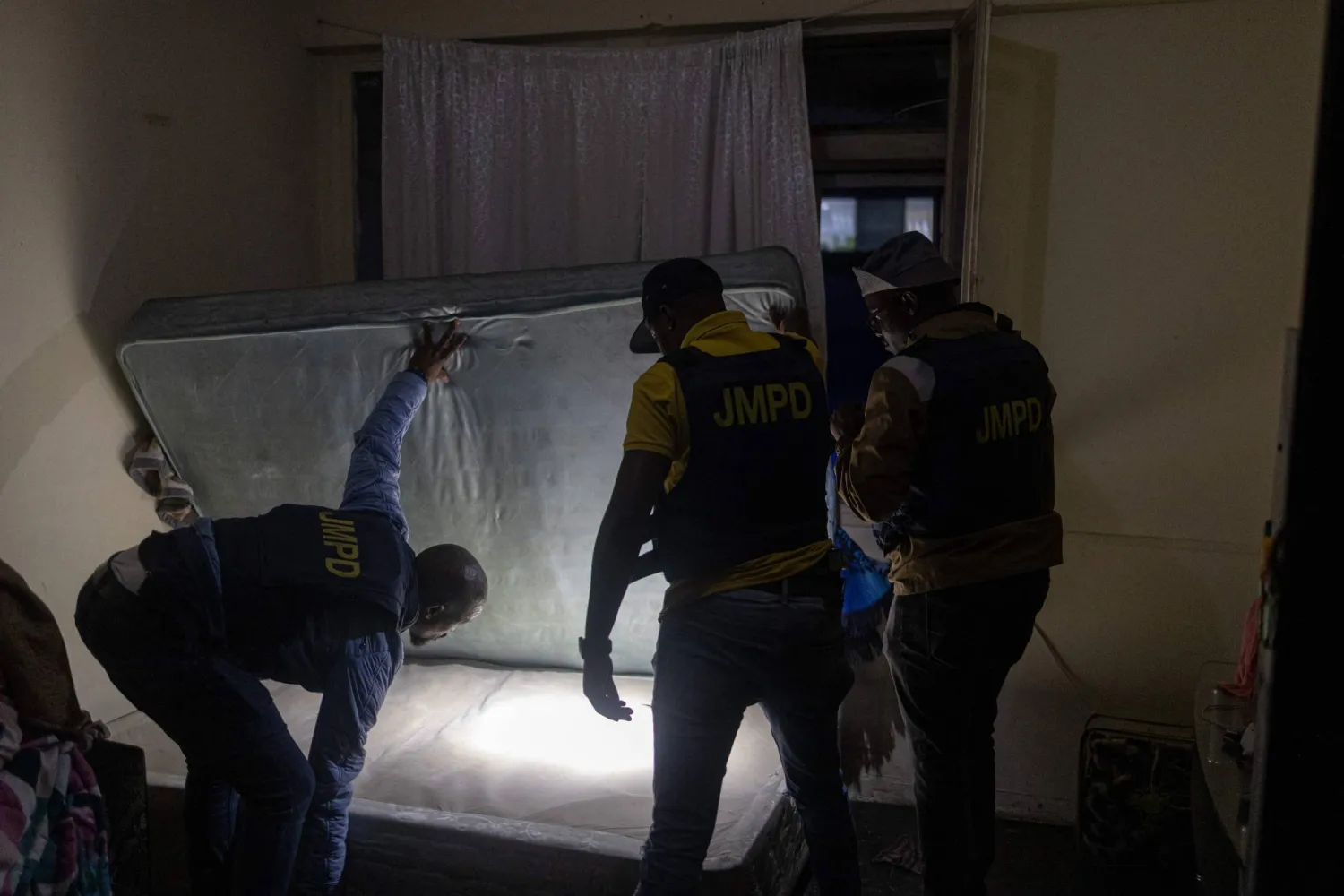 ضباط من إدارة شرطة جوهانسبرج مترو تقوم بتفتيش غرفة نوم خلال مداهمة في مبنى تم الاستيلاء عليه وسط مدينة جوهانسبرج في 18 ديسمبر 2025 (أ.ف.ب)