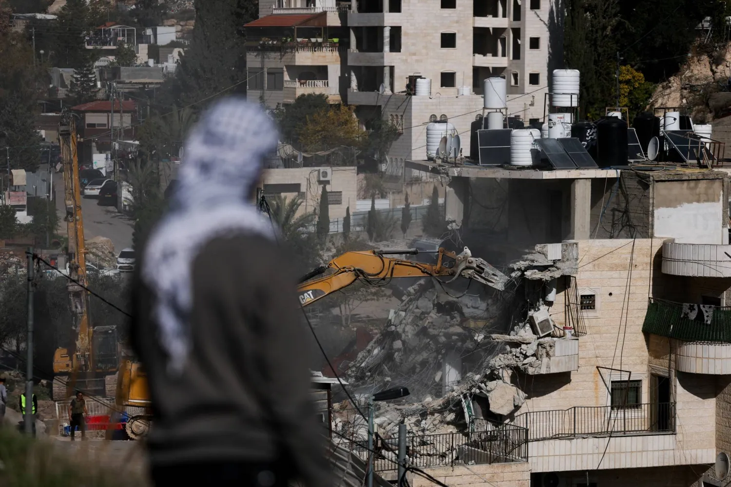 رجل فلسطيني يشاهد القوات الإسرائيلية وهي تهدم المبنى السكني في القدس الشرقية (رويترز)