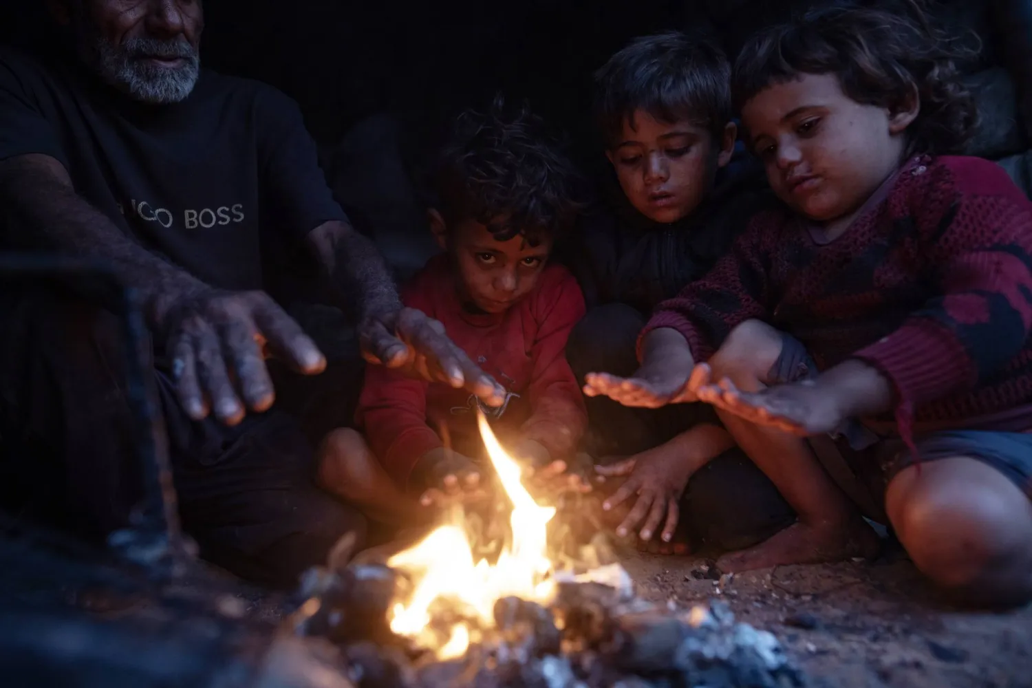 أفراد عائلة فلسطينية نازحة يتدفأون حول نار خارج مأواهم في مدينة خان يونس أمس (إ.ب.أ)
