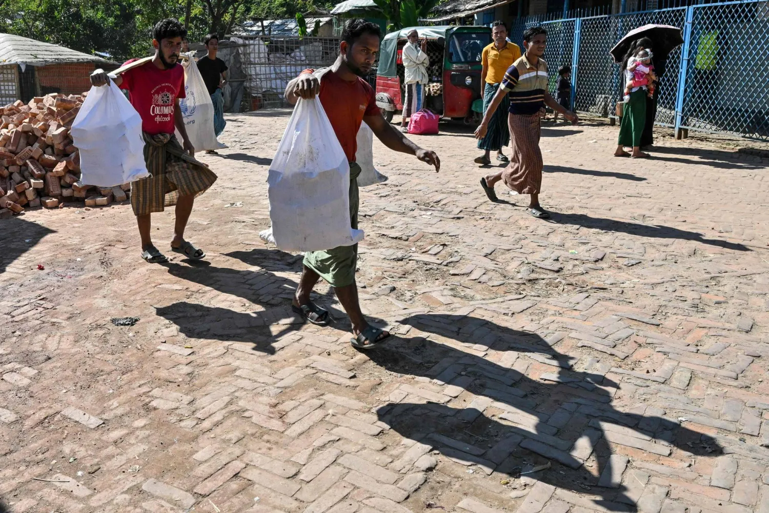 This photograph taken on December 20, 2025 shows Rohingya refugee men carrying bricks at the Kutupalong refugee camp in Cox's Bazar. (AFP)