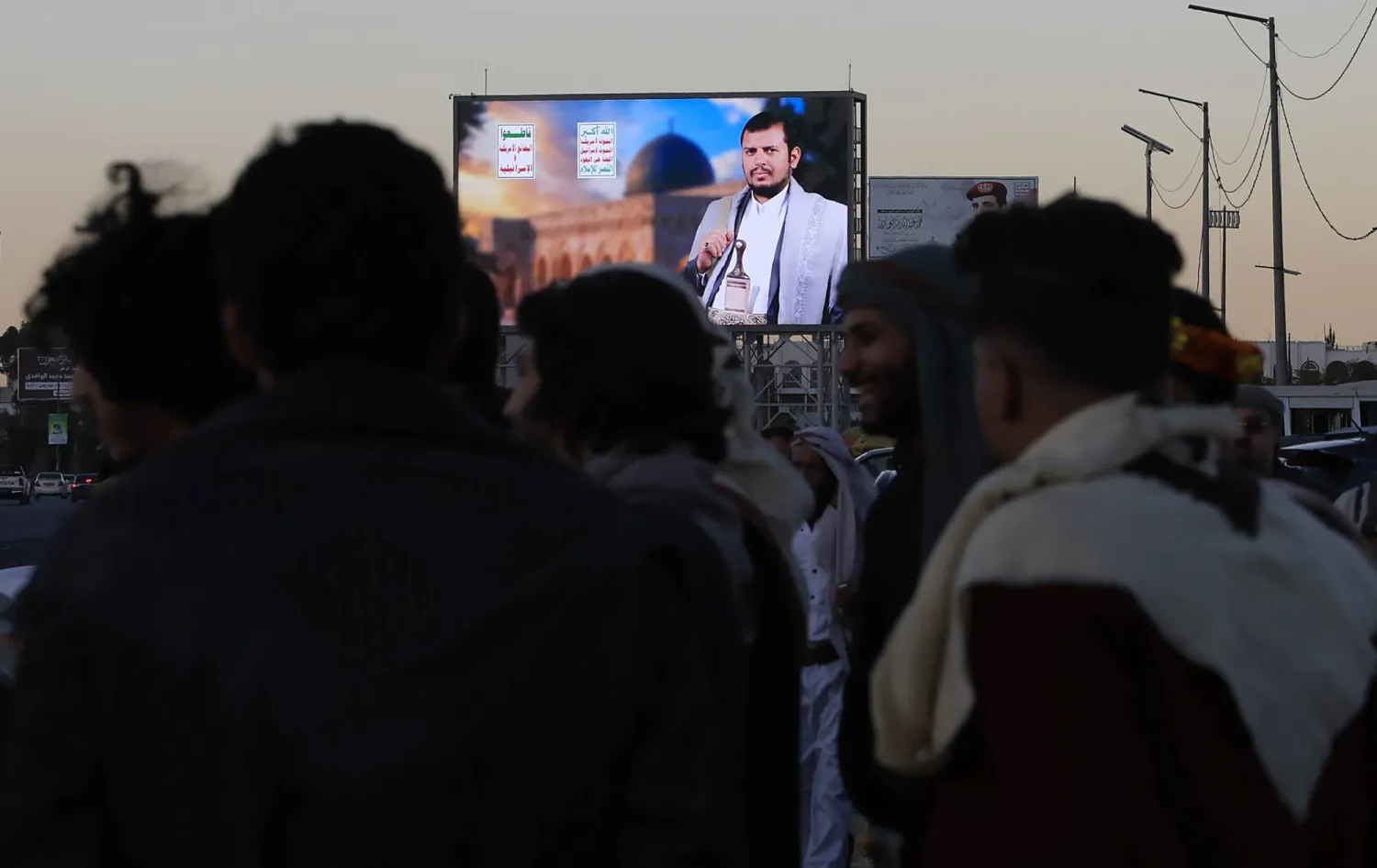 أشخاص متجمعون أمام لوحة إعلانية رقمية في صنعاء تحمل صورة زعيم الحوثيين (إ.ب.أ)