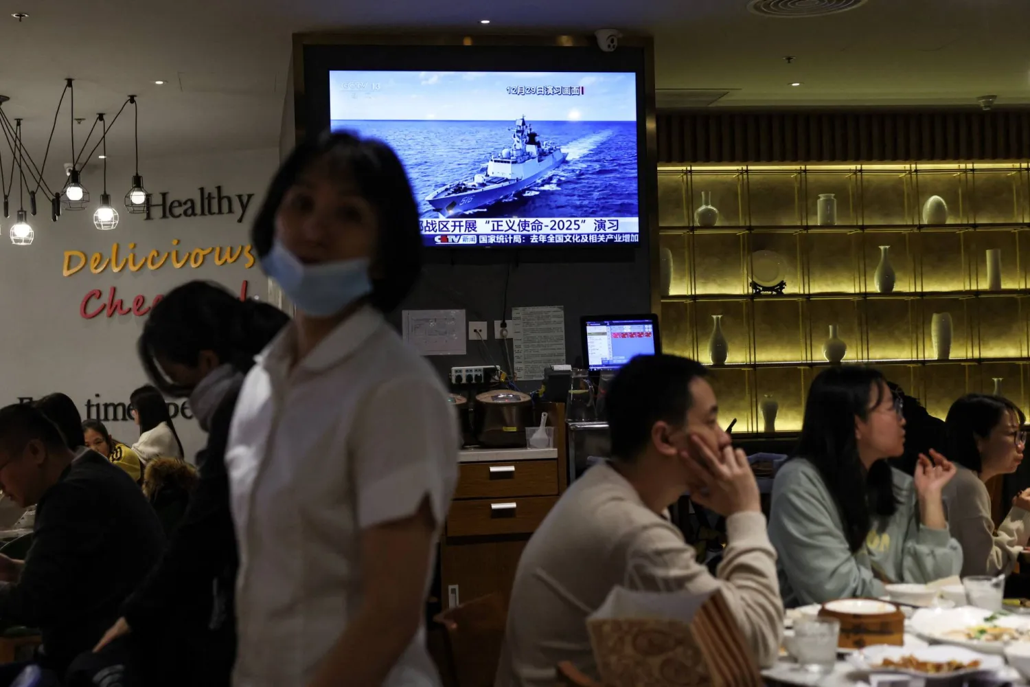 يتناول رواد مطعم في بكين-الصين الطعام بالقرب من شاشة تلفزيون تعرض تقريراً إخبارياً عن مناورات «مهمة العدالة 2025» العسكرية الصينية حول تايوان (رويترز)