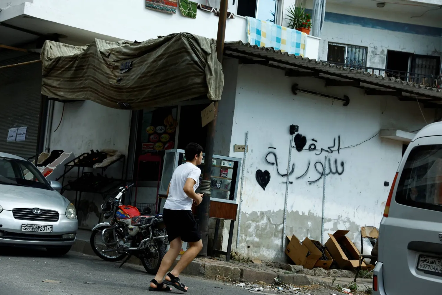 شاب يركض أمام جدار بشعار «سوريا حرة» في القرداحة محافظة اللاذقية سبتمبر الماضي (رويترز)