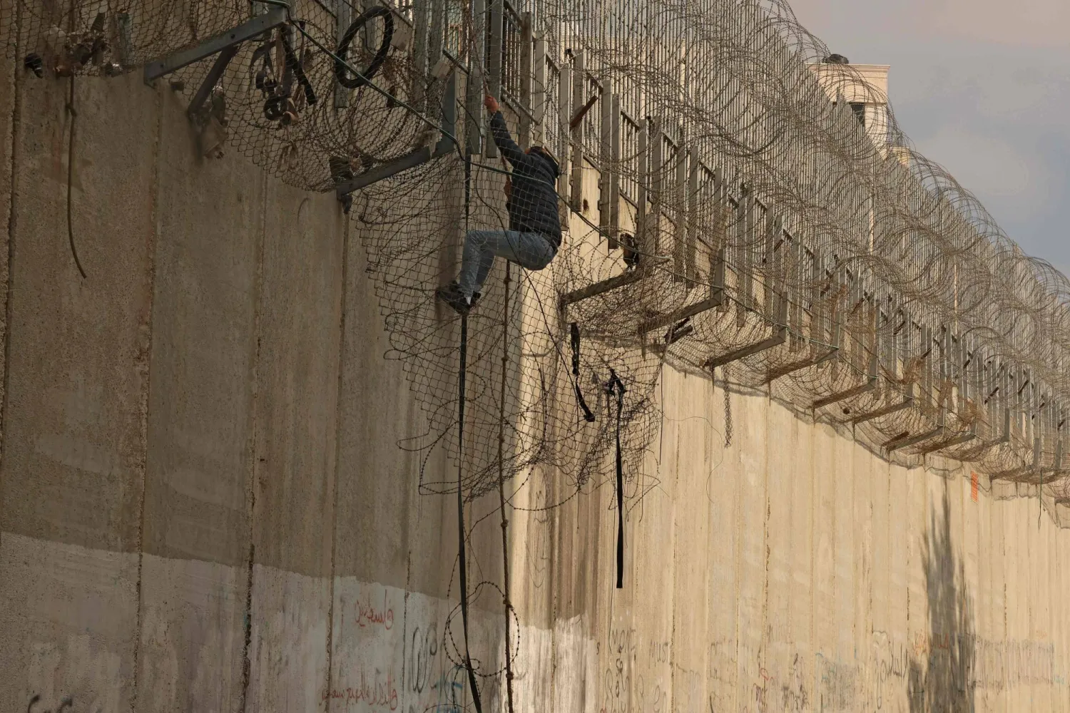 فلسطيني يتسلق جدار الفصل الإسرائيلي الذي يفصل الضفة الغربية عن القدس السبت (أ.ف.ب)