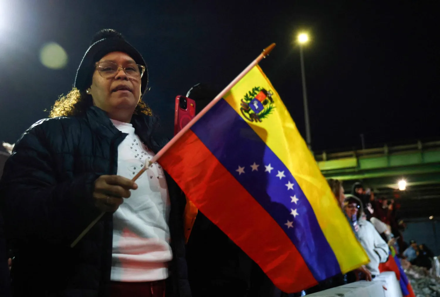 People hold the Venezuelan flag as they celebrate outside the Metropolitan Detention facility in the Brooklyn borough of New York, where ousted president Nicolas Maduro is expected to be held, on January 3, 2026 in New York City.  (Photo by John Lamparski / AFP)