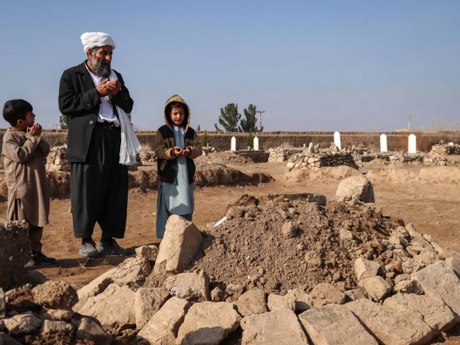 Gul Ahmad (center) along with his deceased stepbrother Habibullah's son Waheed (right) and Saeed offering prayers over his grave in Ghunjan. Mohsen KARIMI / AFP
