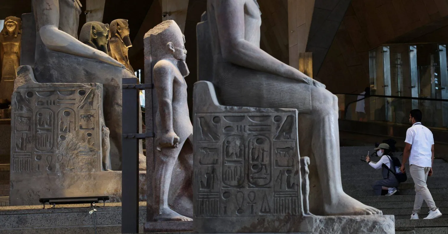 سائحة تلتقط صوراً لتماثيل معروضة داخل المتحف المصري الكبير والذي جذب العديد من السياح في 2025 (رويترز)