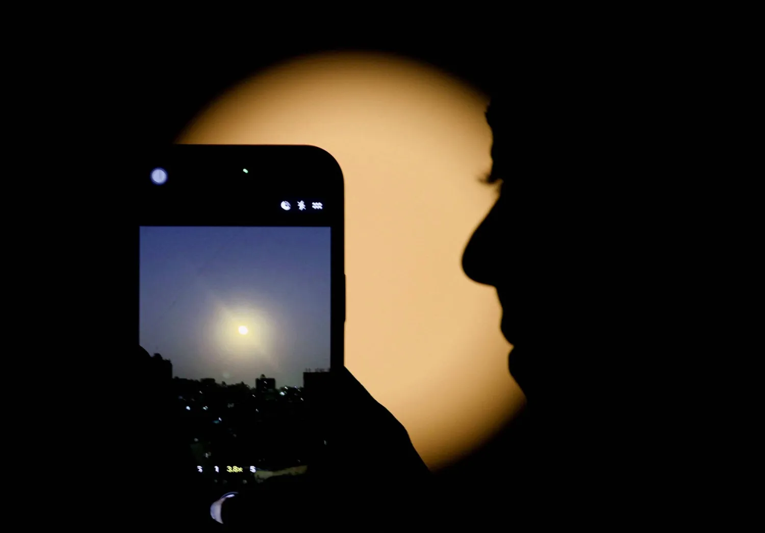 امرأة تستخدم هاتفها الذكي لتصوير قمر الذئب أول قمر عملاق في عام 2026 وهو يضيء سماء القاهرة ليلاً (رويترز)