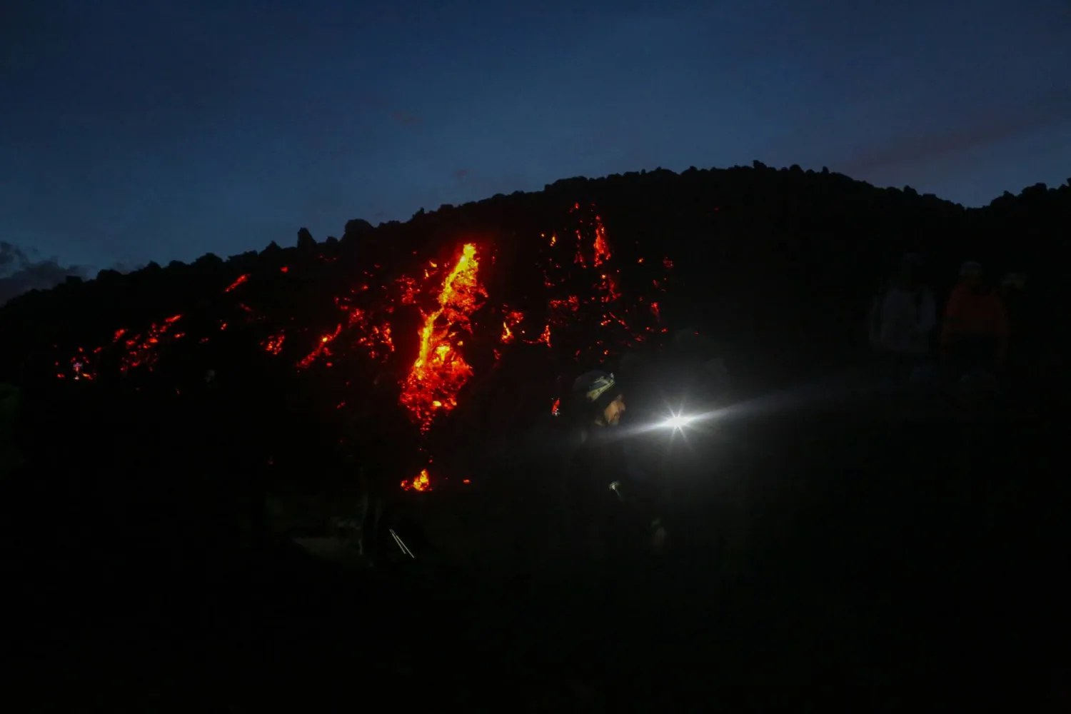 Glowing lava flows across the dark volcanic terrain during nighttime activity on the slopes of Mount Etna during a tour in Catania, Sicily, Italy, January 3, 2026. REUTERS/Antonio Denti