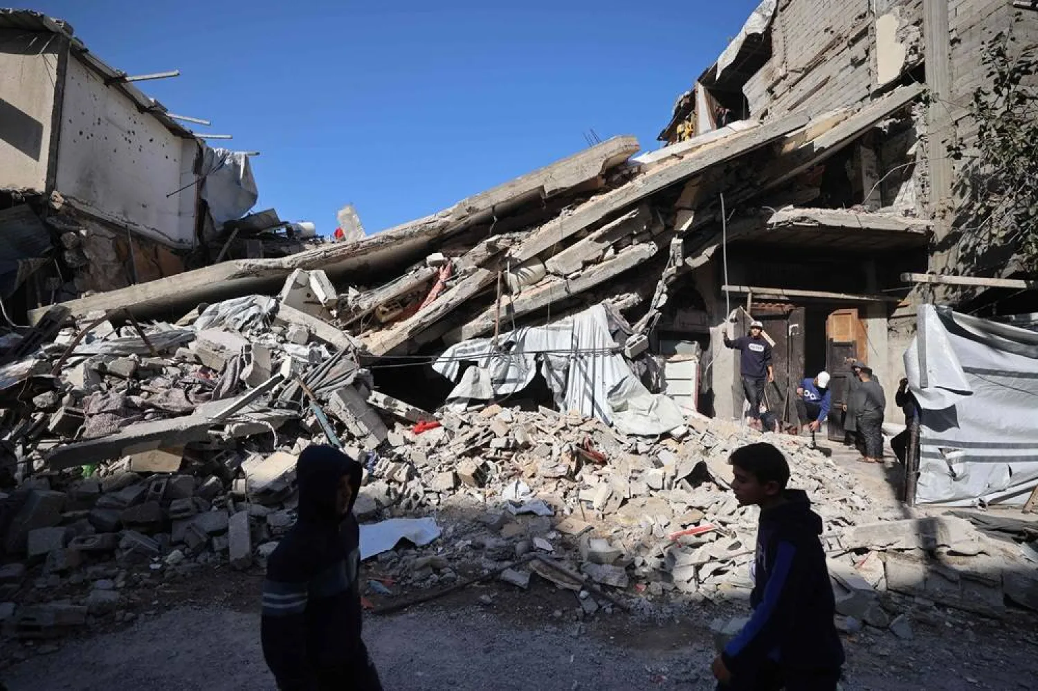 Palestinians walk past the debris of a collapsed house that was previously damaged by an Israeli strike, at the Maghazi refugee camp in the central of Gaza Strip on January 5, 2026. (AFP)