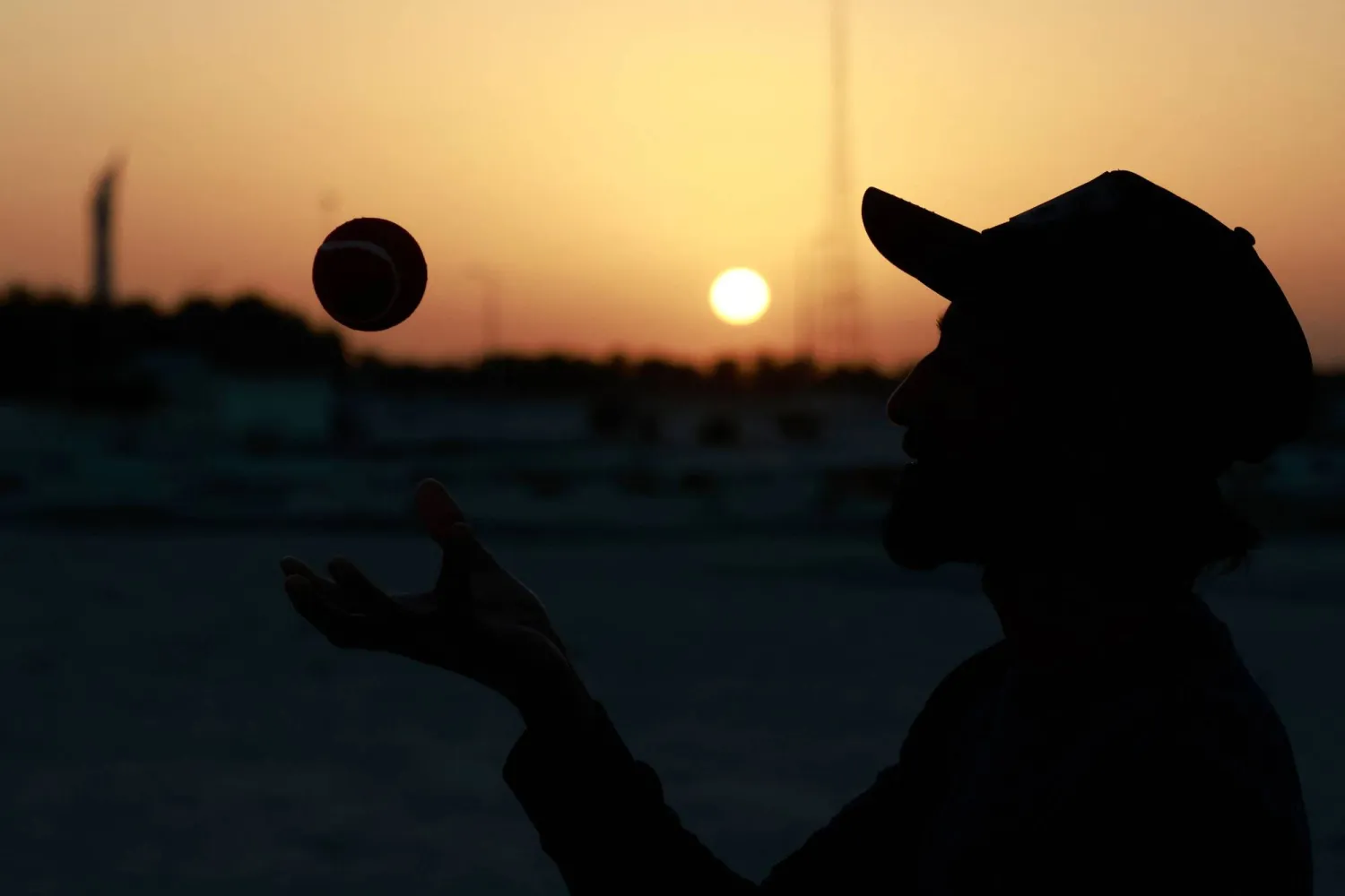 عامل أجنبي يلعب الكريكيت يظهر كظلال أمام غروب الشمس في الدوحة في اليوم الأول من العام الجديد (أ.ف.ب)