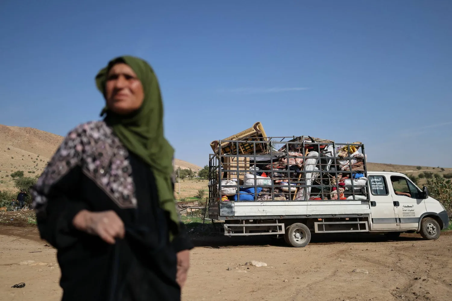 فلسطينية تقف قرب شاحنة تنقل متعلقات عائلاتها التي نزحت قسراً مع عائلات أخرى يوم الخميس من منطقة العوجا البدوية قرب أريحا بالضفة الغربية بعد تصاعد هجمات المستوطنين الإسرائيليين (رويترز)