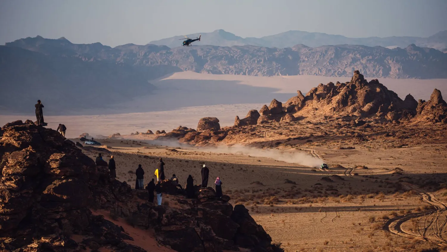 سيارة أحد المتسابقين تشق طريقها في حين يراقب عشاق الرالي المشهد من فوق إحدى الهضاب (الشرق الأوسط)