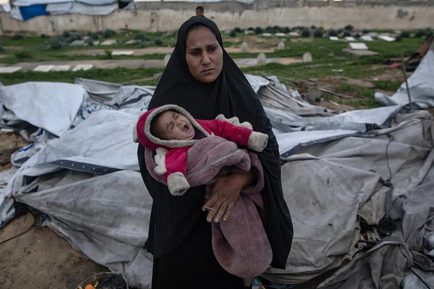 فلسطينية تحمل طفلها الرضيع بعد أن انهارت خيمتها في خان يونس جنوب قطاع غزة جراء الرياح القوية والأمطار (إ.ب.أ)