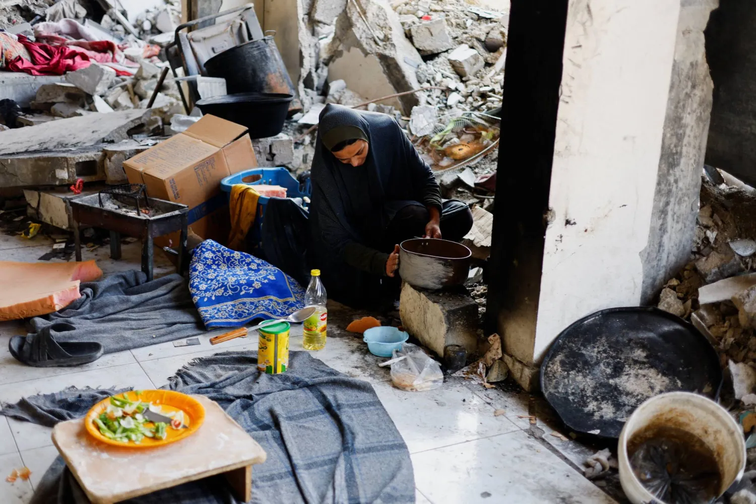 فلسطينية تطهو الطعام بين حطام منزلها في غزة (رويترز)
