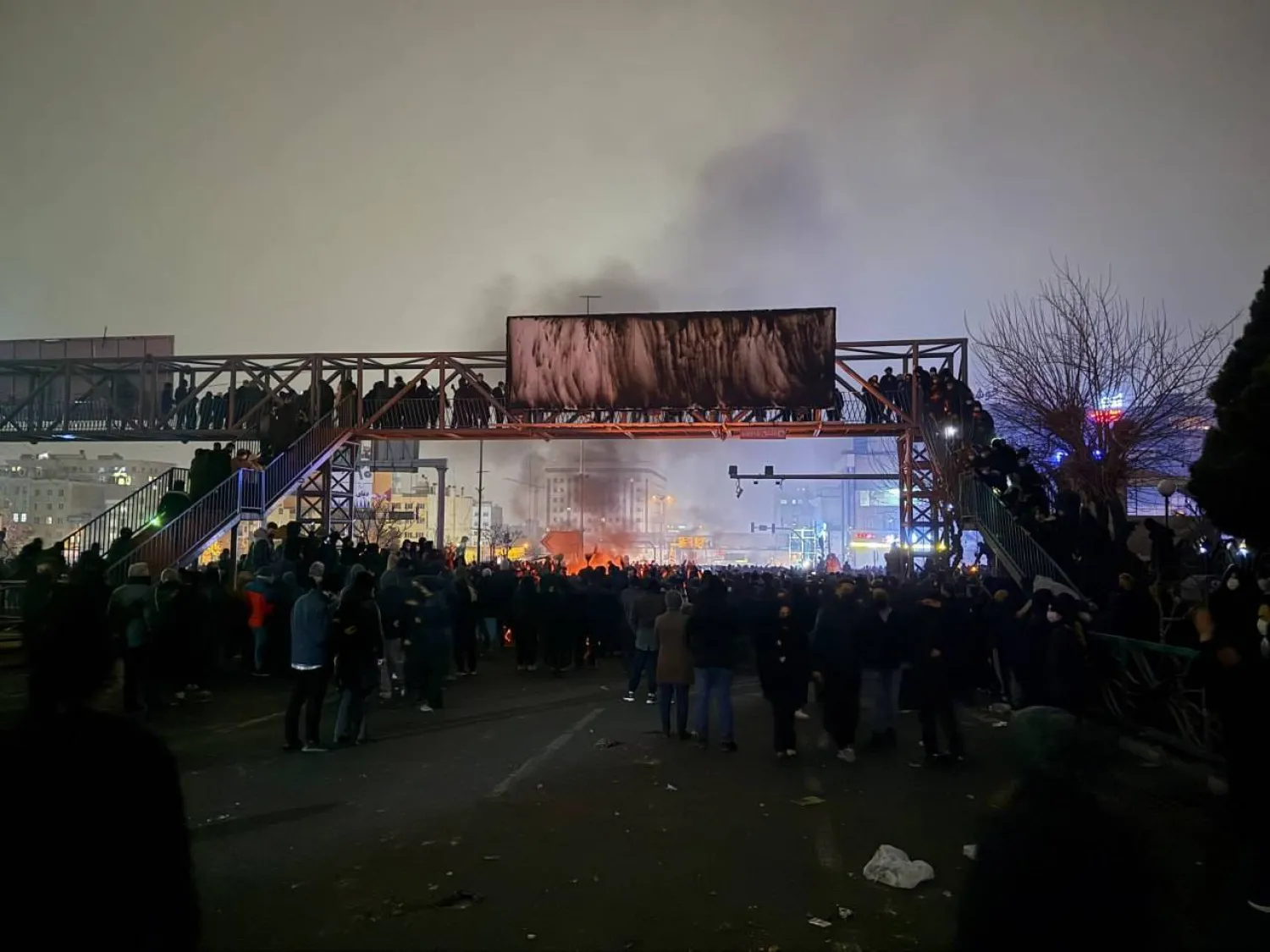 محتجون يحرقون لافتة معلقة فوق جسر للمشاة في حي بونك شمال غربي طهران الجمعة (تلغرام)