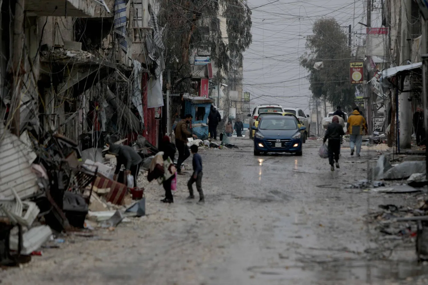 People walk down a street as a car drives by following a ceasefire which ended days of fighting between Syrian security forces and Kurdish fighters in the Kurdish-majority Sheikh Maqsoud neighborhood, of the northern city of Aleppo on January 11, 2026. (AFP)