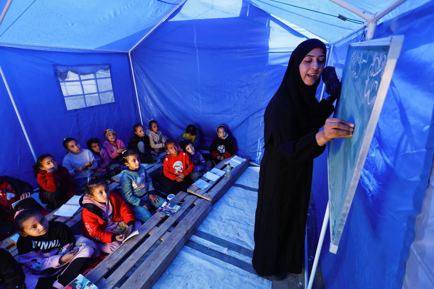 
أطفال فلسطينيون نازحون يتلقون الدروس داخل خيمة قرب الخط الفاصل بين «حماس» وإسرائيل في بيت لاهيا شمال غزة (رويترز)