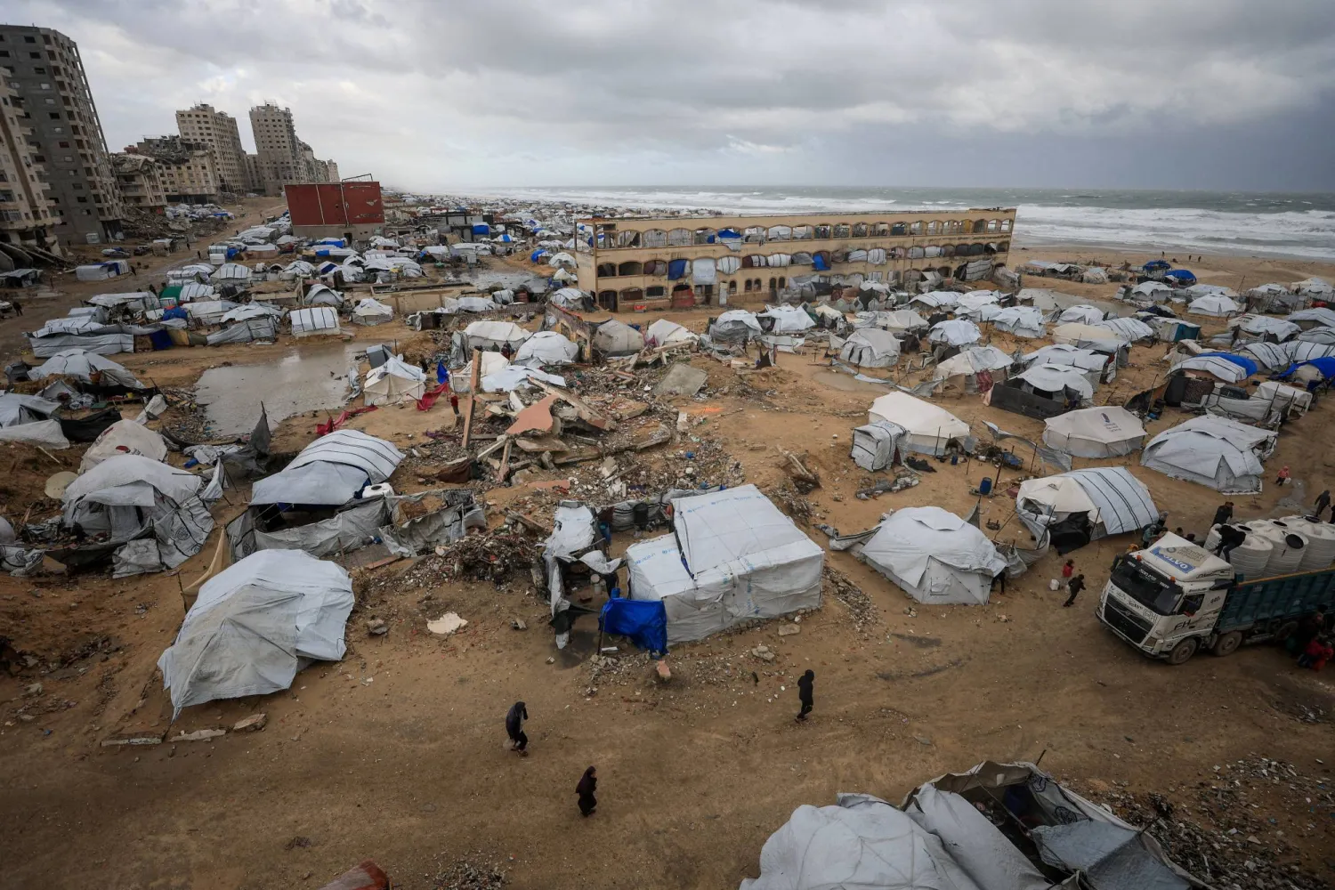 Palestinians walk past tents used by displaced people, during a windy winter day, in Gaza City, January 13, 2026. (Reuters)