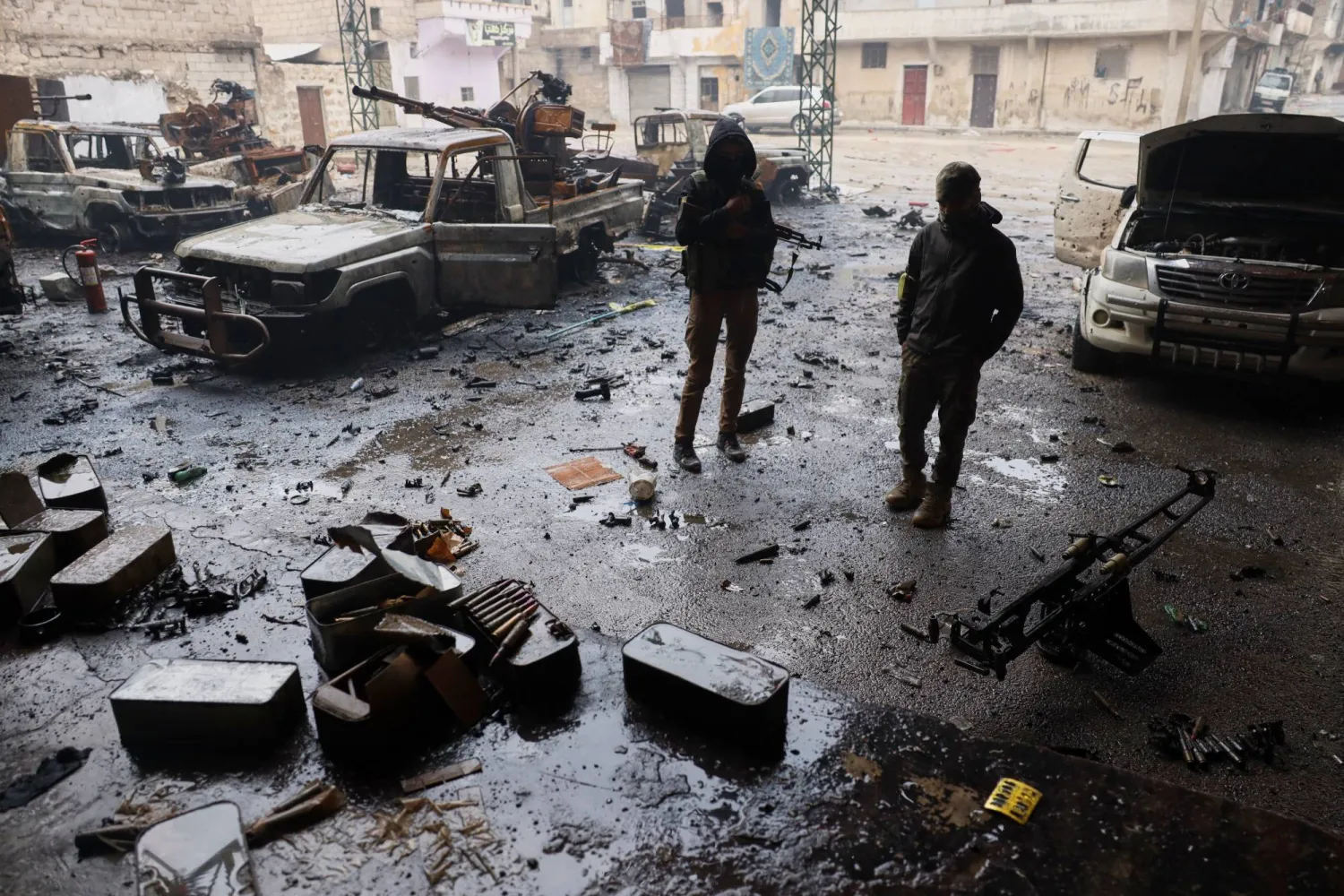 عناصر من قوات الأمن السورية يقفون بجوار مركبات محترقة وذخيرة ملقاة على الأرض في حي الشيخ مقصود حيث اندلعت الاشتباكات الثلاثاء 6 يناير بين القوات الحكومية وقوات سوريا الديمقراطية (قسد) التي يقودها الأكراد بمدينة حلب السورية - 12 يناير 2026 (أ.ب)
