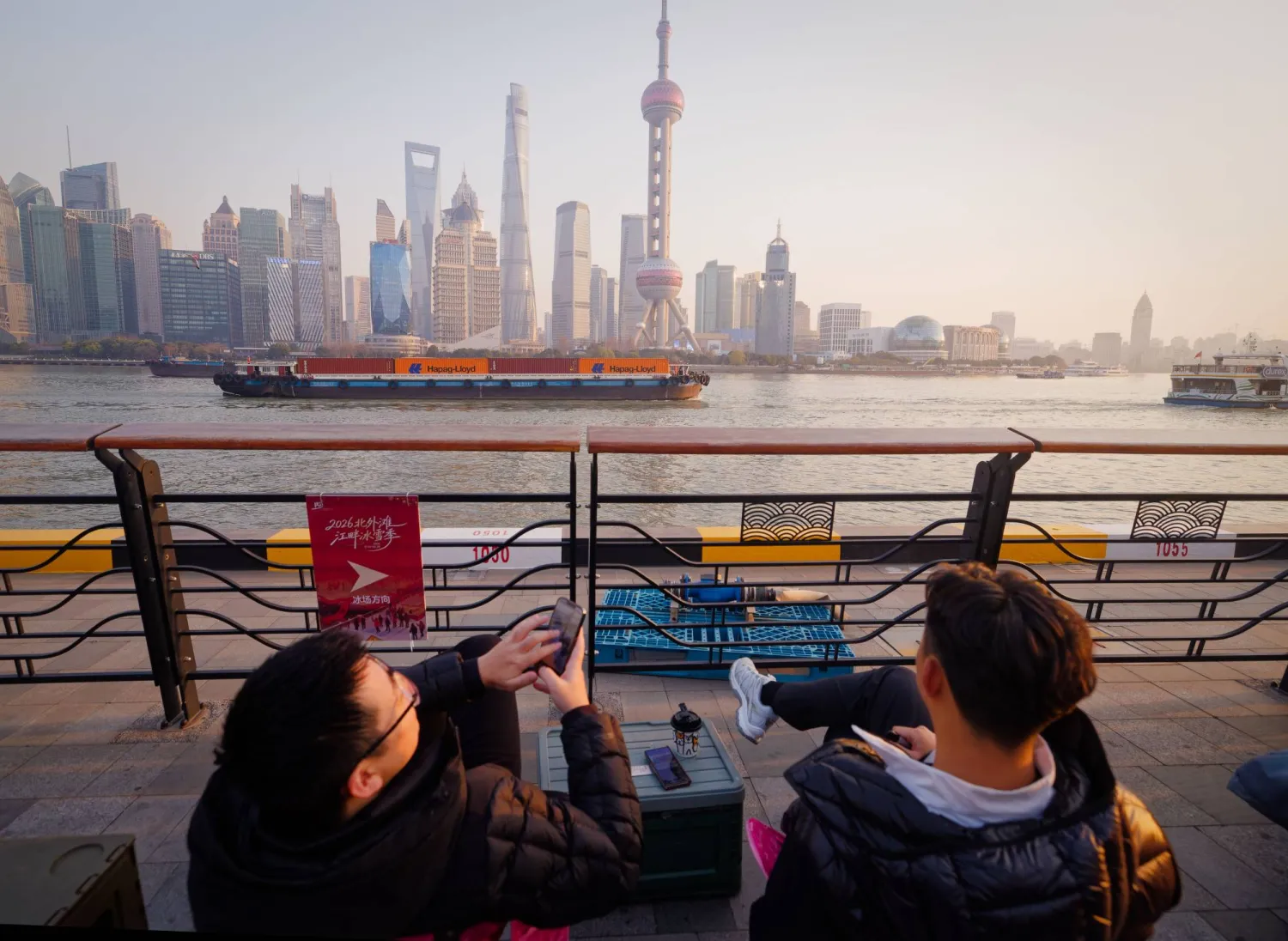 رواد مقهى يشاهدون سفن شحن تعبر نهر هوانغبو في شنغهاي (إ.ب.أ)