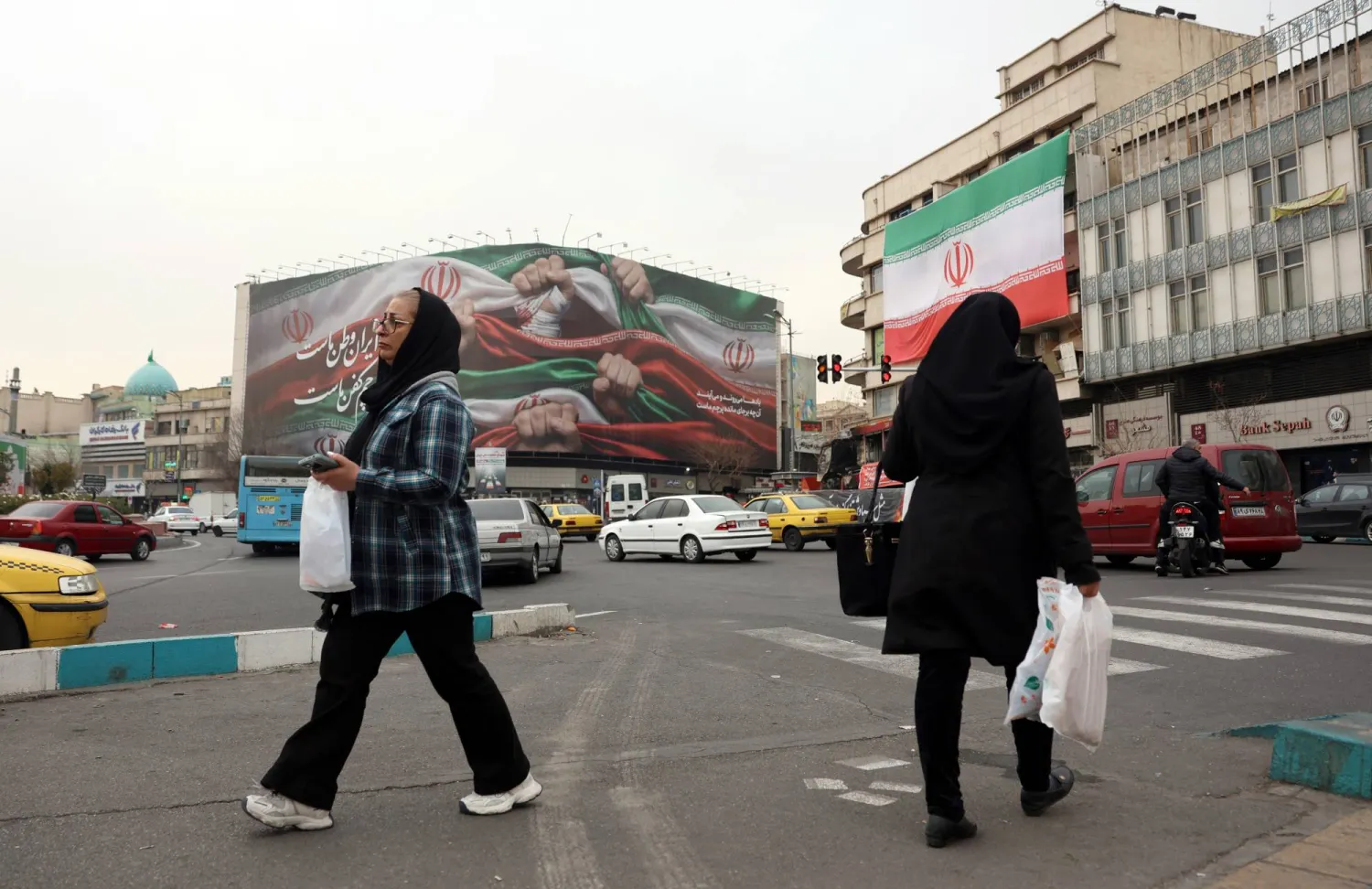 Iranians walk next to a billboard reading "Iran is our Homeland" at Enqelab Square in Tehran, Iran, 13 January 2026. (EPA)