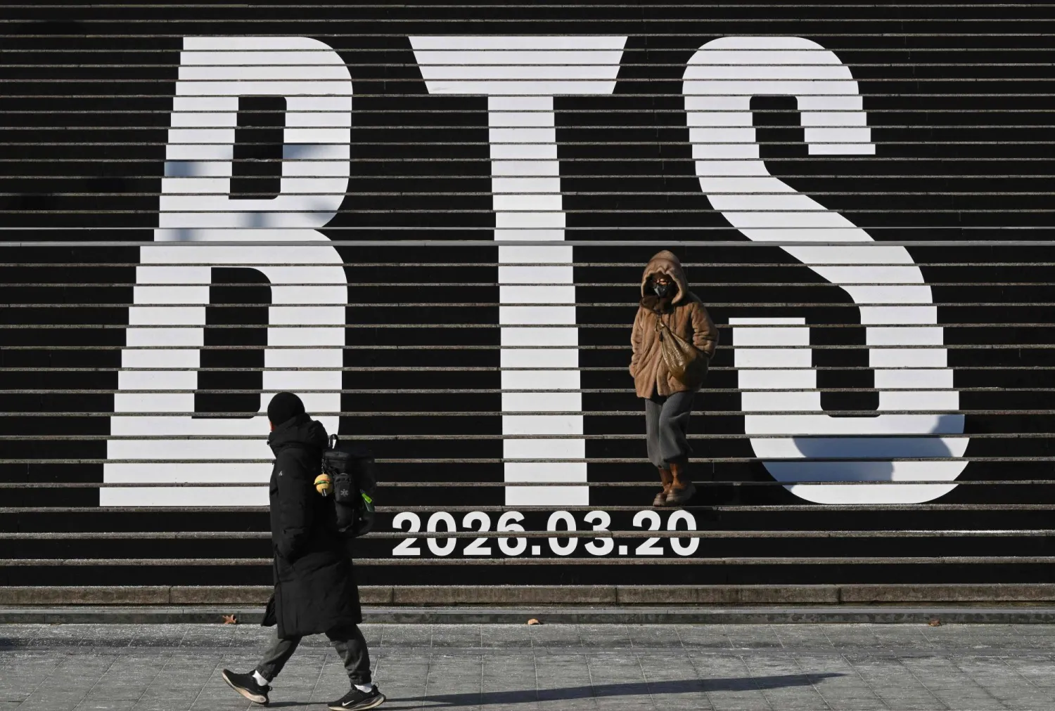 Pedestrians walk along the stairs displayed with the BTS logo and release date of BTS' 2026 album at Gwanghwamun Square in Seoul on January 14, 2026. (AFP)