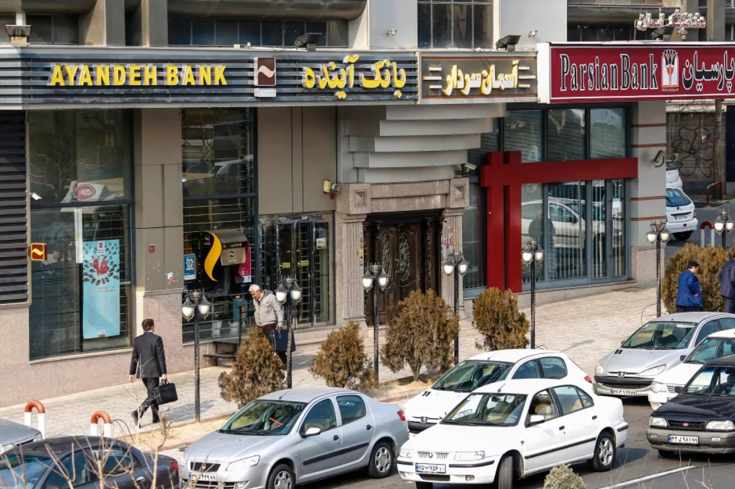 إيرانيون يمرون أمام أحد فروع بنك «آينده» عام 2017 (أ.ف.ب)